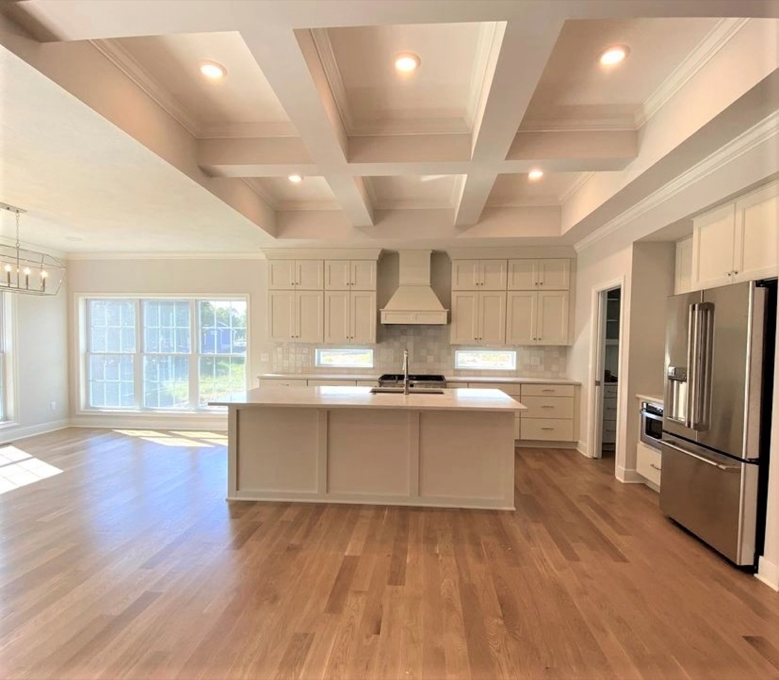 Open-concept model kitchen with coffered ceiling, greige cabinets and large island by Kitchen Express, Syracuse NY