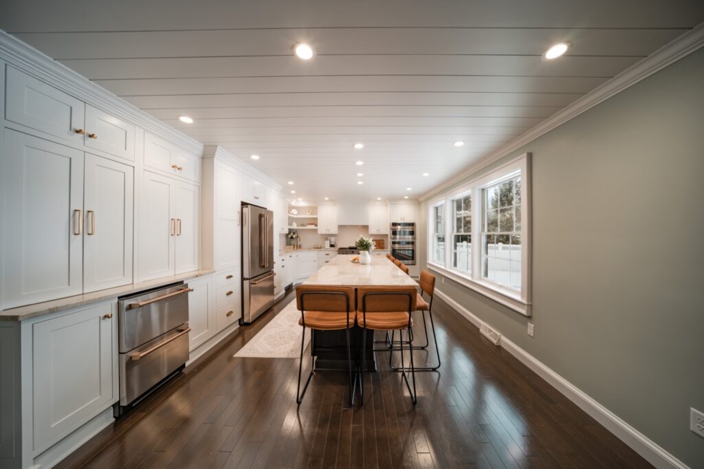 Bright transitional kitchen with white cabinets, gray island, marble counters and shiplap ceiling by Kitchen Express, Syracuse NY