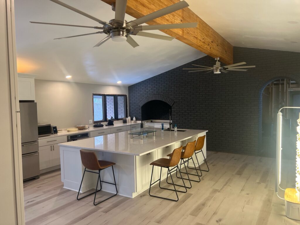 Open-concept modern kitchen with vaulted beamed ceiling, white waterfall island and charcoal brick wall by Kitchen Express, Syracuse NY