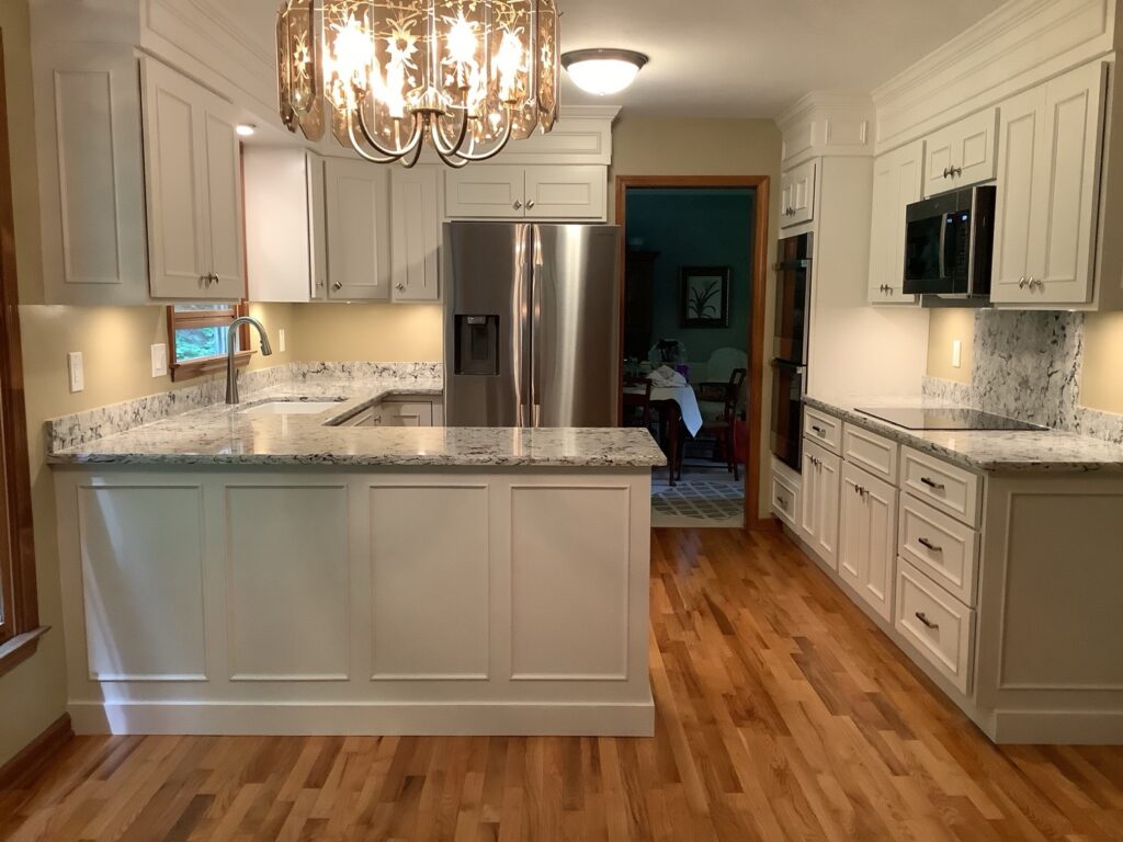 Elegant cream painted kitchen with granite counters, marble backsplash and statement chandelier by Kitchen Express, Syracuse NY